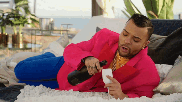 a man in a pink jacket is laying on a bed with a bottle of champagne