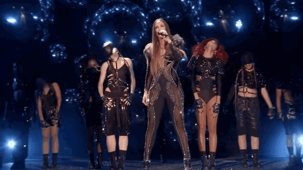 a woman singing into a microphone while surrounded by dancers