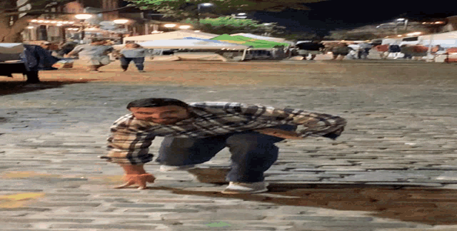 a man in a plaid shirt is kneeling down on a cobblestone street