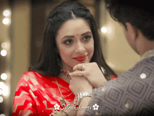 a woman in a red saree is holding a man 's hand and the words maanhearts are on the bottom right