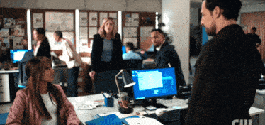a man and a woman are standing in front of a computer screen that says ' cw ' on it