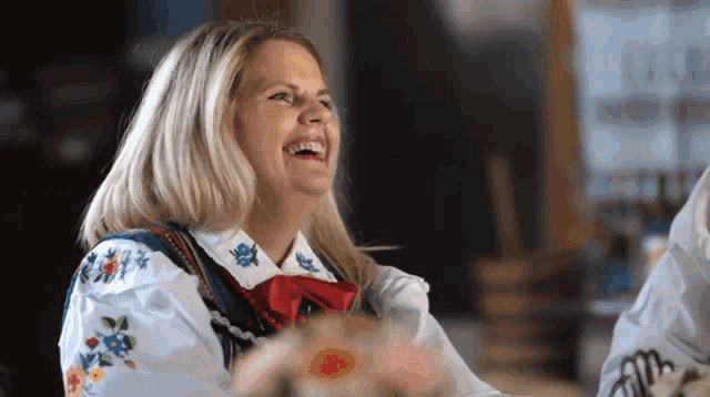 a woman wearing a white shirt with embroidered flowers is laughing