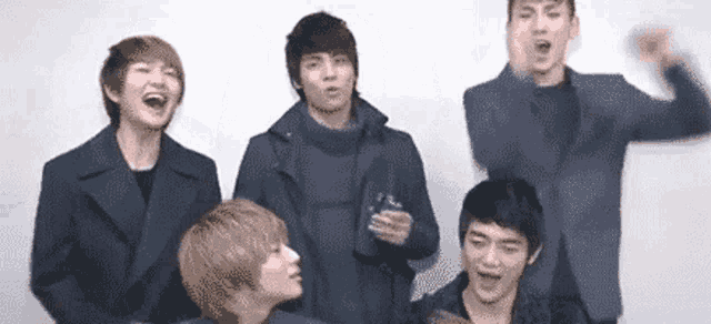a group of young men are standing next to each other in front of a white wall and laughing .