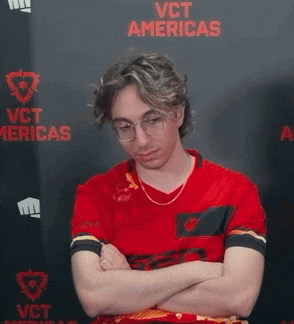 a man in a red shirt is sitting in front of a wall that says vct americas