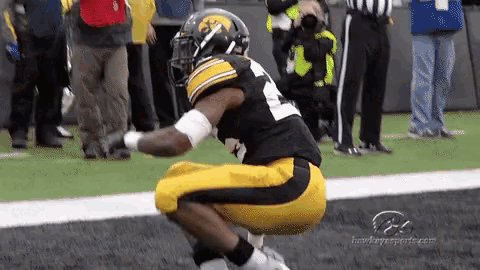 a football player is squatting down on the field while a referee looks on
