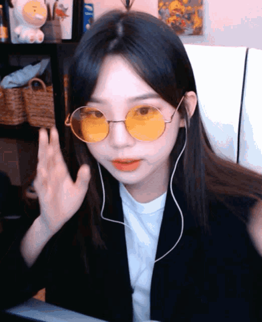 a girl wearing yellow sunglasses and ear buds waves her hand