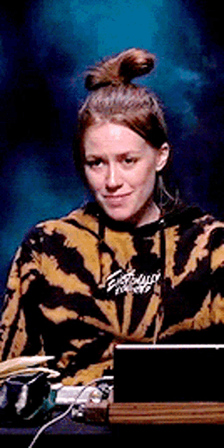 a woman wearing a tie dye hoodie is sitting at a table