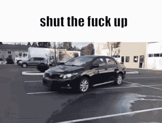 a black car is parked in a parking lot and the words shut the fuck up are above it