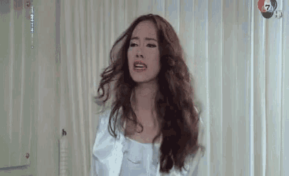 a woman with long hair is standing in front of a white curtain in a room .