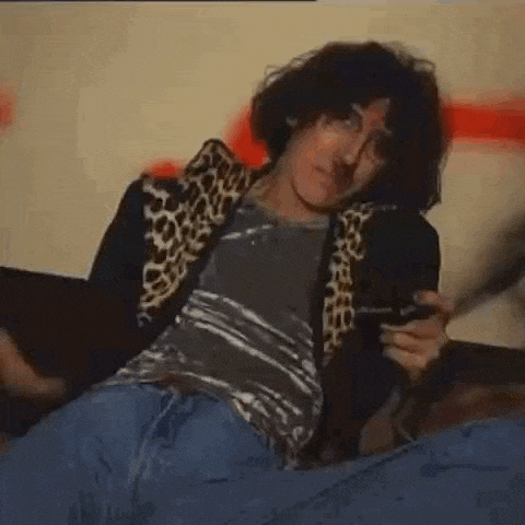 a man with curly hair is sitting on a couch holding a cigarette .