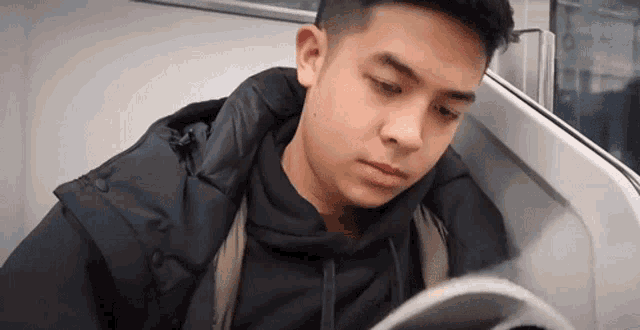 a young man is reading a book while riding a train .