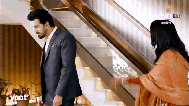 a man in a suit stands next to a woman in a red dress in front of a set of stairs that says voot