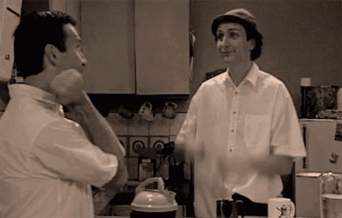 two men are standing in a kitchen and talking to each other .
