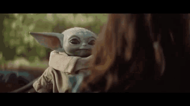 a baby yoda toy is sitting next to a woman .