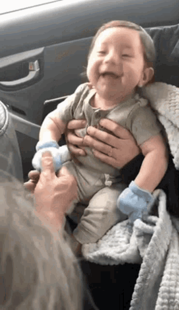 a baby is smiling while being held by a person in a car seat