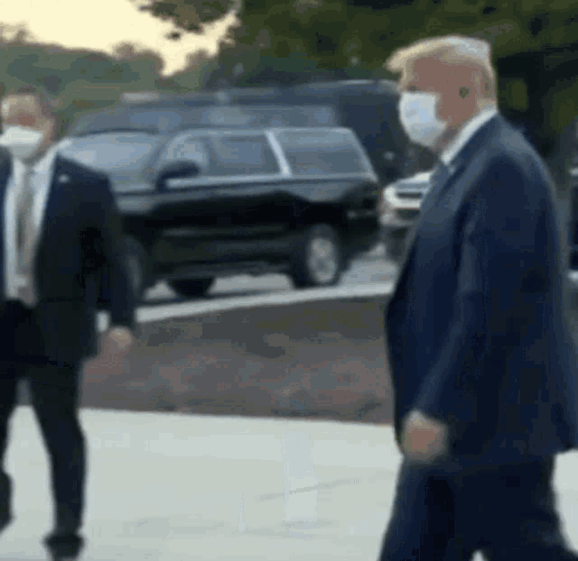 a man in a suit and tie is wearing a face mask while walking down the street .