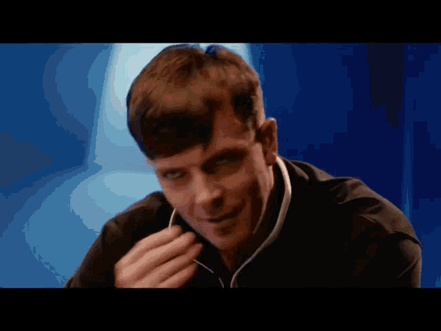 a man wearing ear buds looks at the camera with a blue background