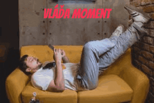 a man is laying on a yellow couch with his legs crossed while holding a cell phone .