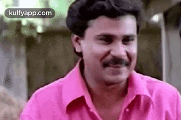 a man wearing a pink shirt and a mustache is smiling .