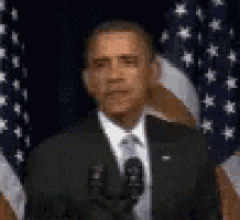 barack obama is giving a speech in front of a microphone in front of an american flag .