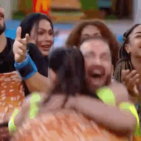 a group of people are laughing and hugging each other while a man is giving a thumbs up .