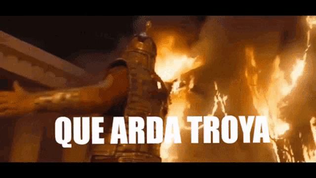 a man in armor is standing in front of a fire with the words que arda troya written below him