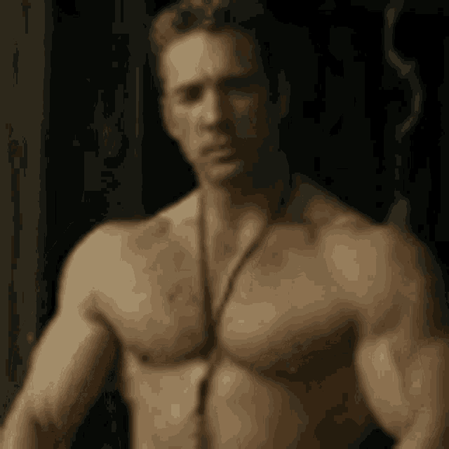 a shirtless man wearing a necklace is standing in a dark room .
