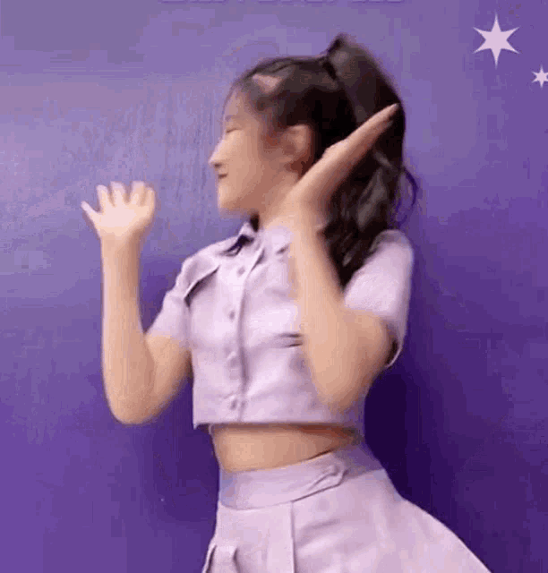 a woman in a purple shirt and skirt is dancing in front of a blue wall .