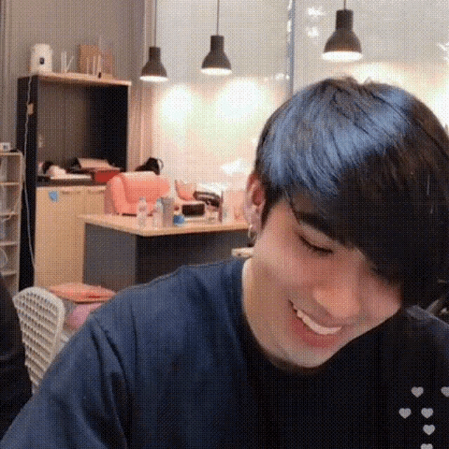 a young man is smiling while sitting at a table in a room with a kitchen in the background .