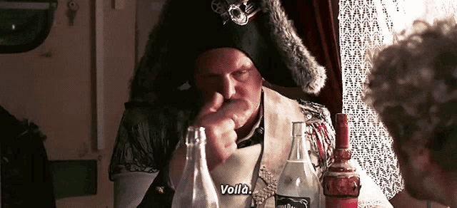 a man in a pirate costume is sitting at a table with a bottle of jack daniels
