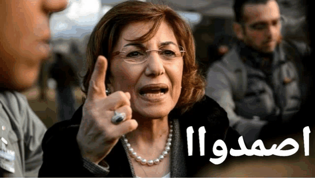 a woman wearing glasses and a pearl necklace is pointing her finger at something