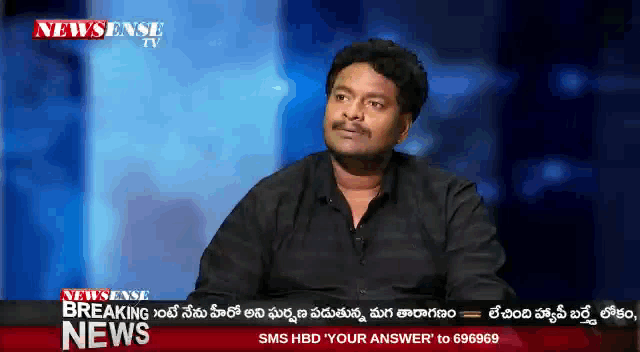 a man is sitting in front of a news screen