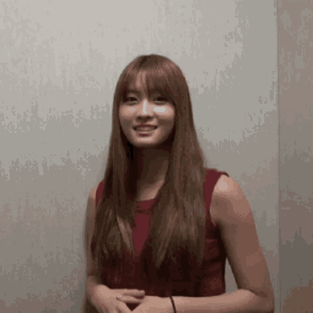 a woman in a red tank top is smiling while standing in front of a wall
