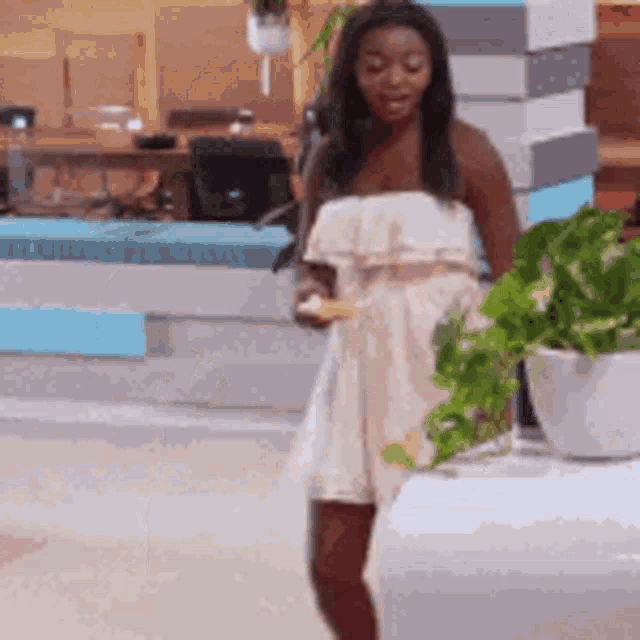 a woman in a white dress is standing next to a potted plant in a living room .