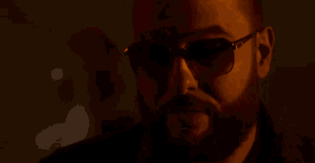 a man wearing sunglasses is smoking a cigarette in a dark room