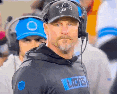 a man wearing headphones and a hat with a lion on it is standing on the sidelines of a football game .