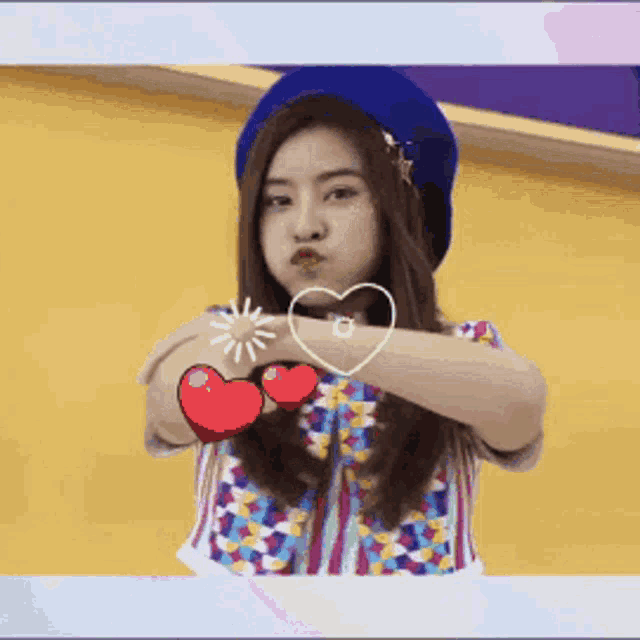 a girl in a blue hat is holding two red hearts