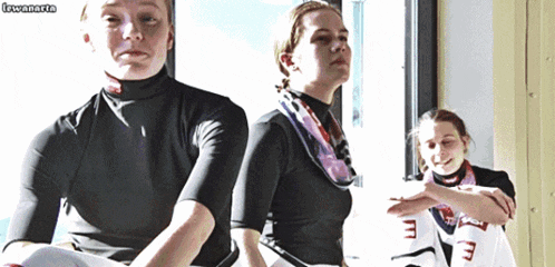 three women are sitting in front of a window and one of them has a scarf around her neck that says ' m '