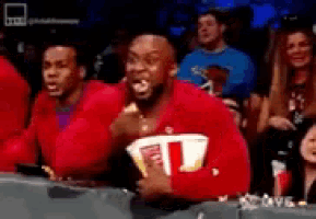 a man in a red shirt is eating popcorn while sitting in a stadium .