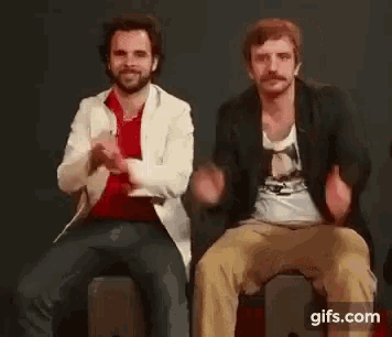 two men are sitting next to each other and clapping their hands together .