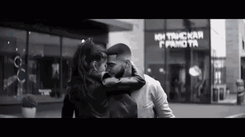 a man and woman are kissing in front of a building in a black and white photo .