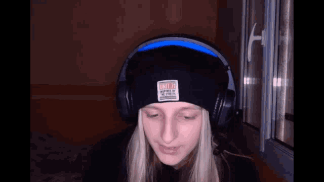 a woman wearing headphones and a beanie looks at the camera