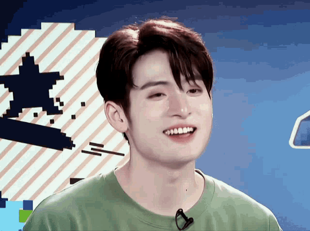 a young man wearing a green shirt is smiling in front of a blue background