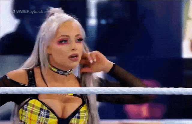 a woman in a plaid top is standing in a wrestling ring with the words wwe payback on the bottom