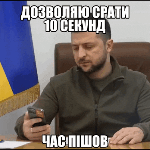 a man is sitting at a desk looking at his cell phone with a foreign language caption