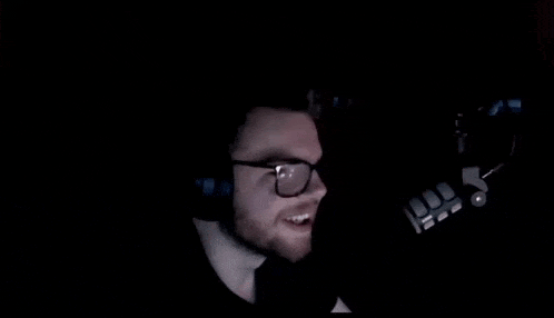a man wearing glasses and headphones is screaming into a microphone in the dark .