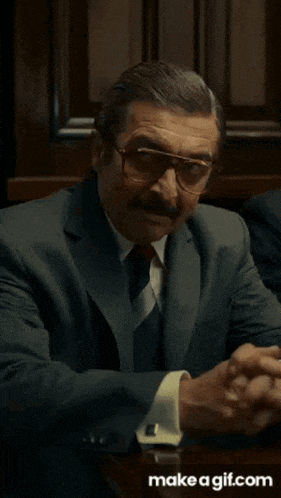 a man in a suit and tie is sitting at a table with his hands in the air .
