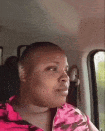 a woman in a pink shirt is sitting in the back seat of a car looking out the window .