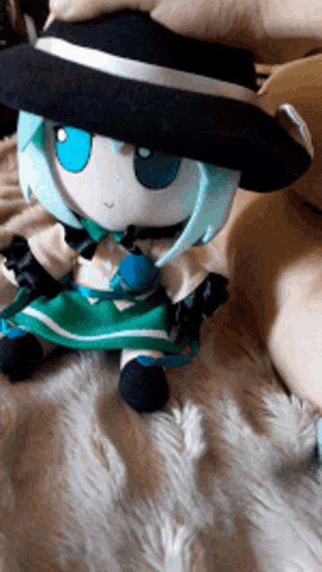 a stuffed doll wearing a black hat and green dress is sitting on a bed