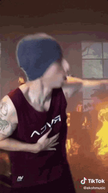 a man wearing a tank top with the word eva on it is standing in front of a fire